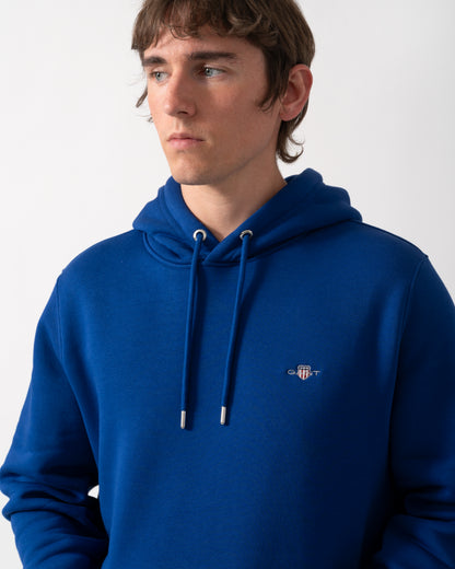 close up shot of a model wearing a GANT Mens Regular Fit Shield Logo Pullover Hoodie in 435 Crisp Blue