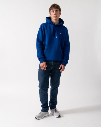 full length shot of a model wearing a GANT Mens Regular Fit Shield Logo Pullover Hoodie in 435 Crisp Blue