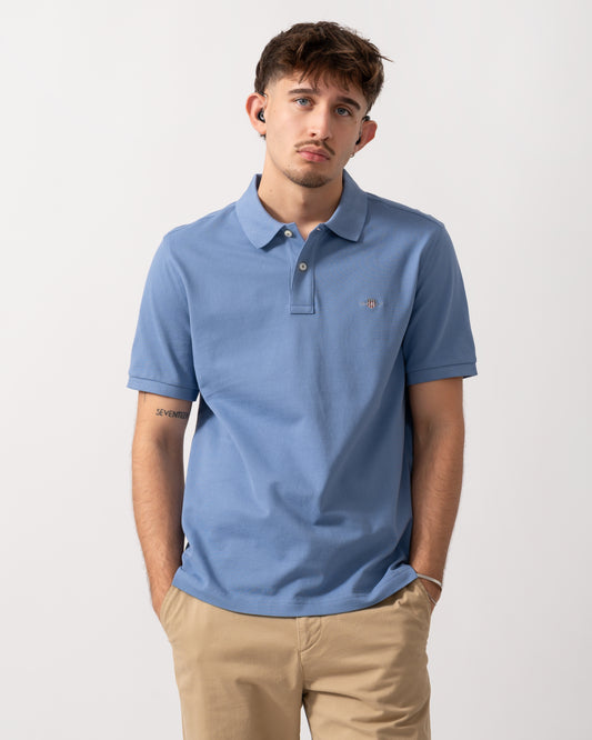 Model wearing a GANT Mens Regular Fit Short Sleeve Shield Logo Pique Polo in Faded Denim