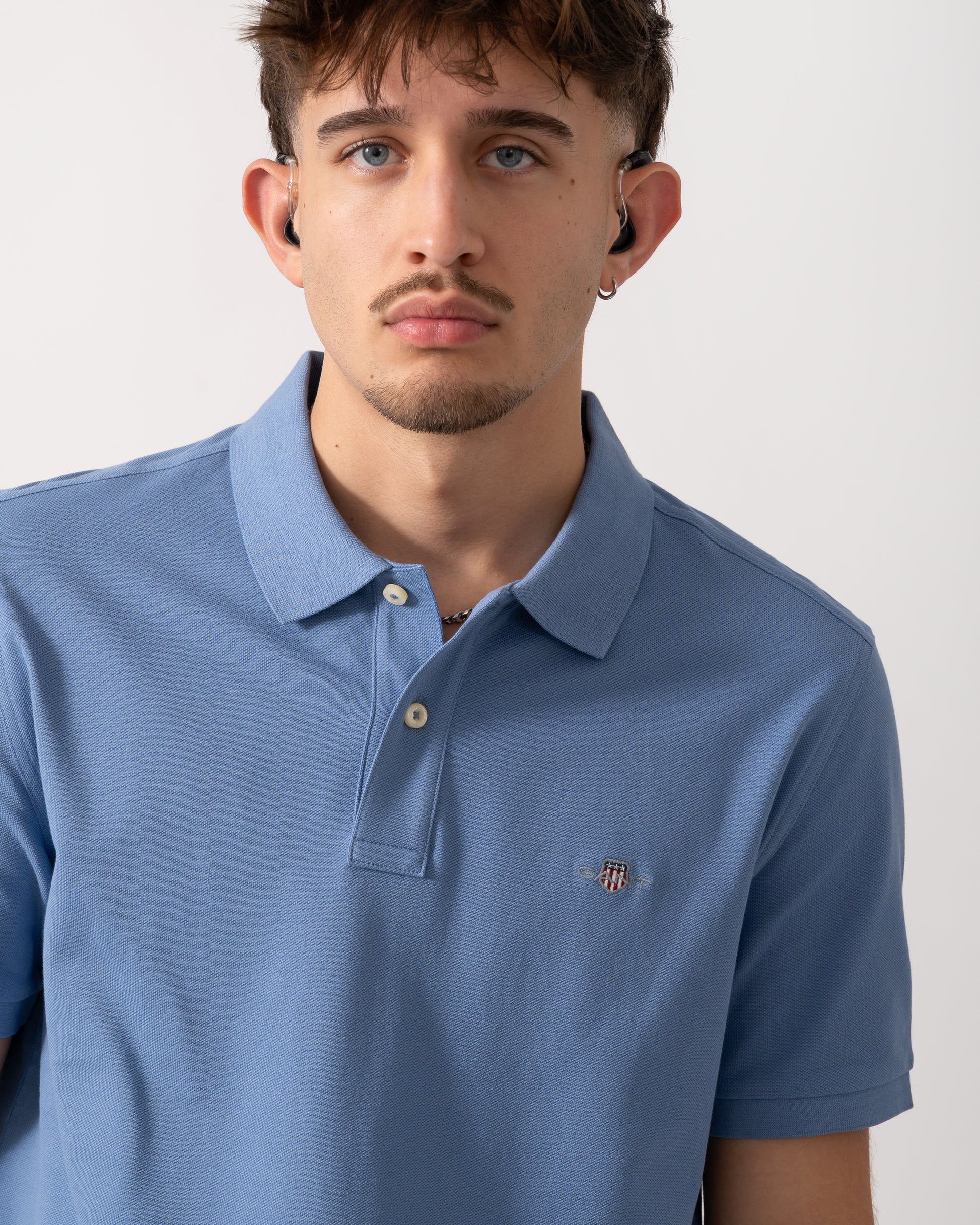 Close up shot of a Model wearing a GANT Mens Regular Fit Short Sleeve Shield Logo Pique Polo in Faded Denim