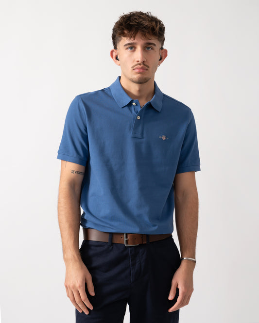 Model wearing a GANT Mens Regular Fit Short Sleeve Shield Logo Pique Polo in Vintage Blue
