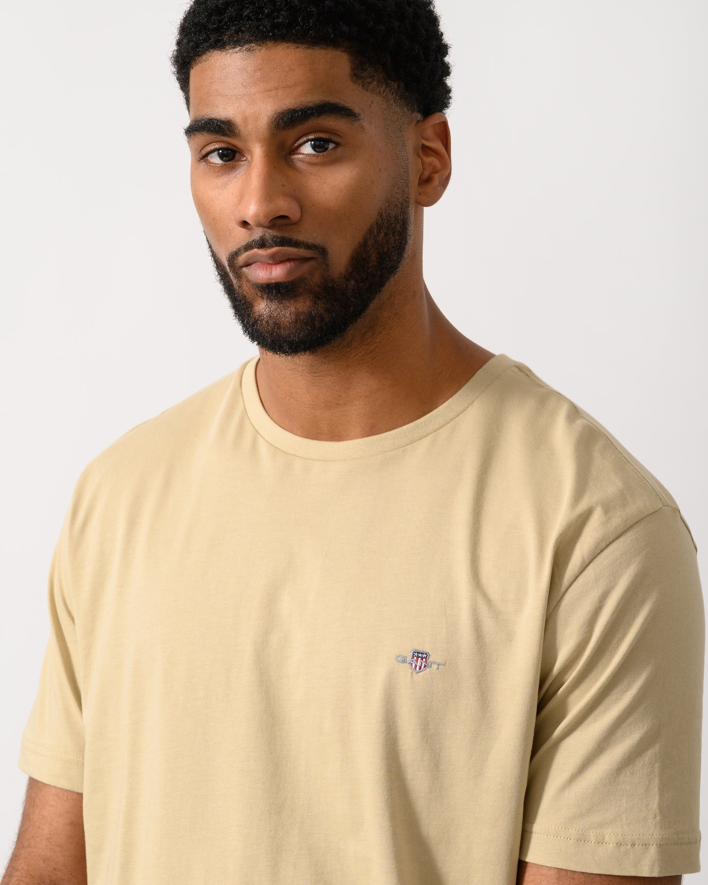 detail shot of a model wearing a GANT Mens Regular Fit Short Sleeve Shield Logo T-Shirt in Oat Beige