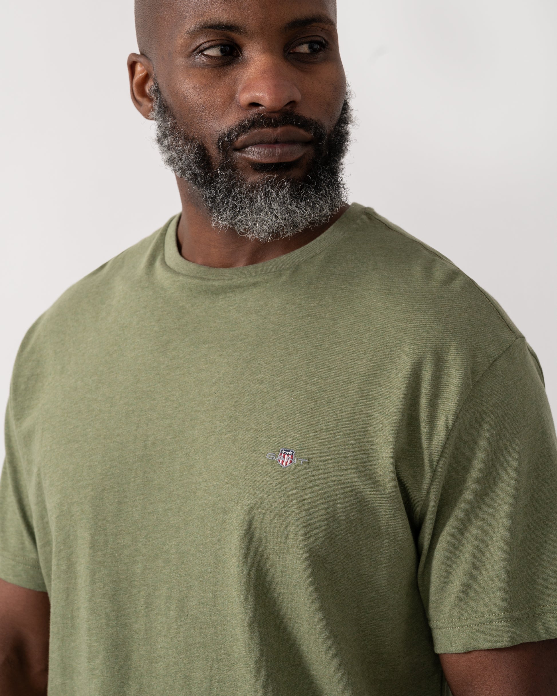 detail shot a a model wearing a GANT Mens Regular Fit Short Sleeve Shield Logo T-Shirt in Dark Cactus Melange