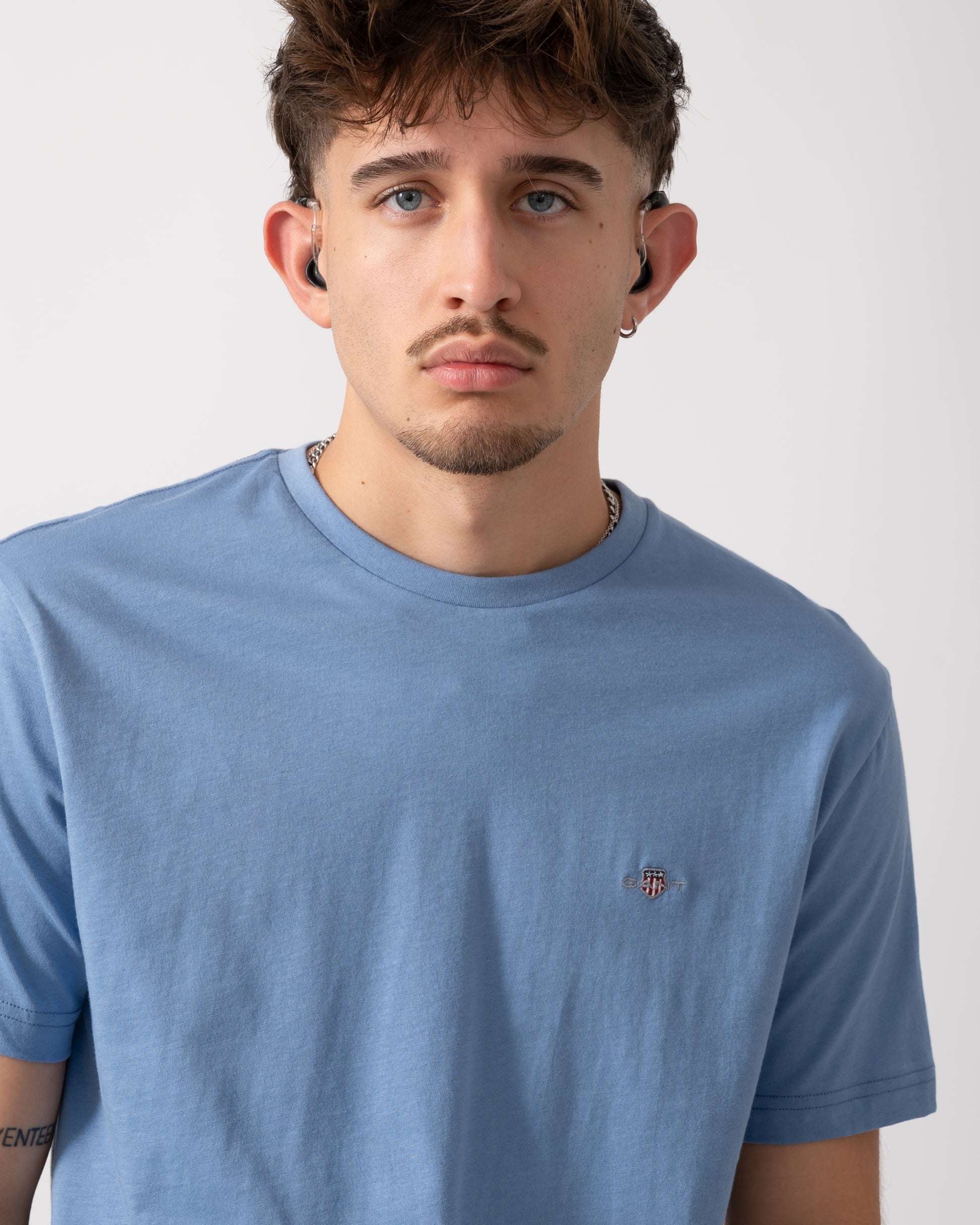 close up of a Model wearing a GANT Mens Regular Fit Short Sleeve Shield Logo T-Shirt in Faded Denim