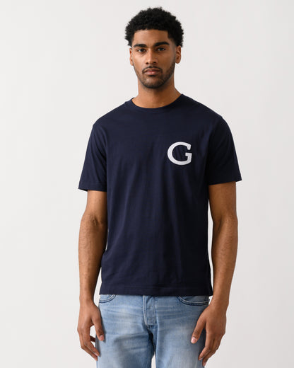 Model wearing a GANT Mens Short Sleeve G-Badge T-Shirt in 433 Evening Blue
