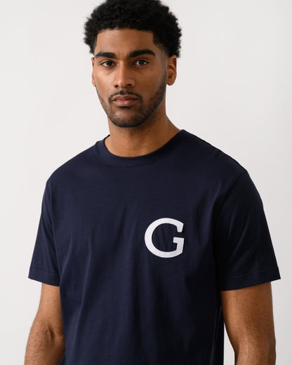 close up shot of aModel wearing a GANT Mens Short Sleeve G-Badge T-Shirt in 433 Evening Blue
