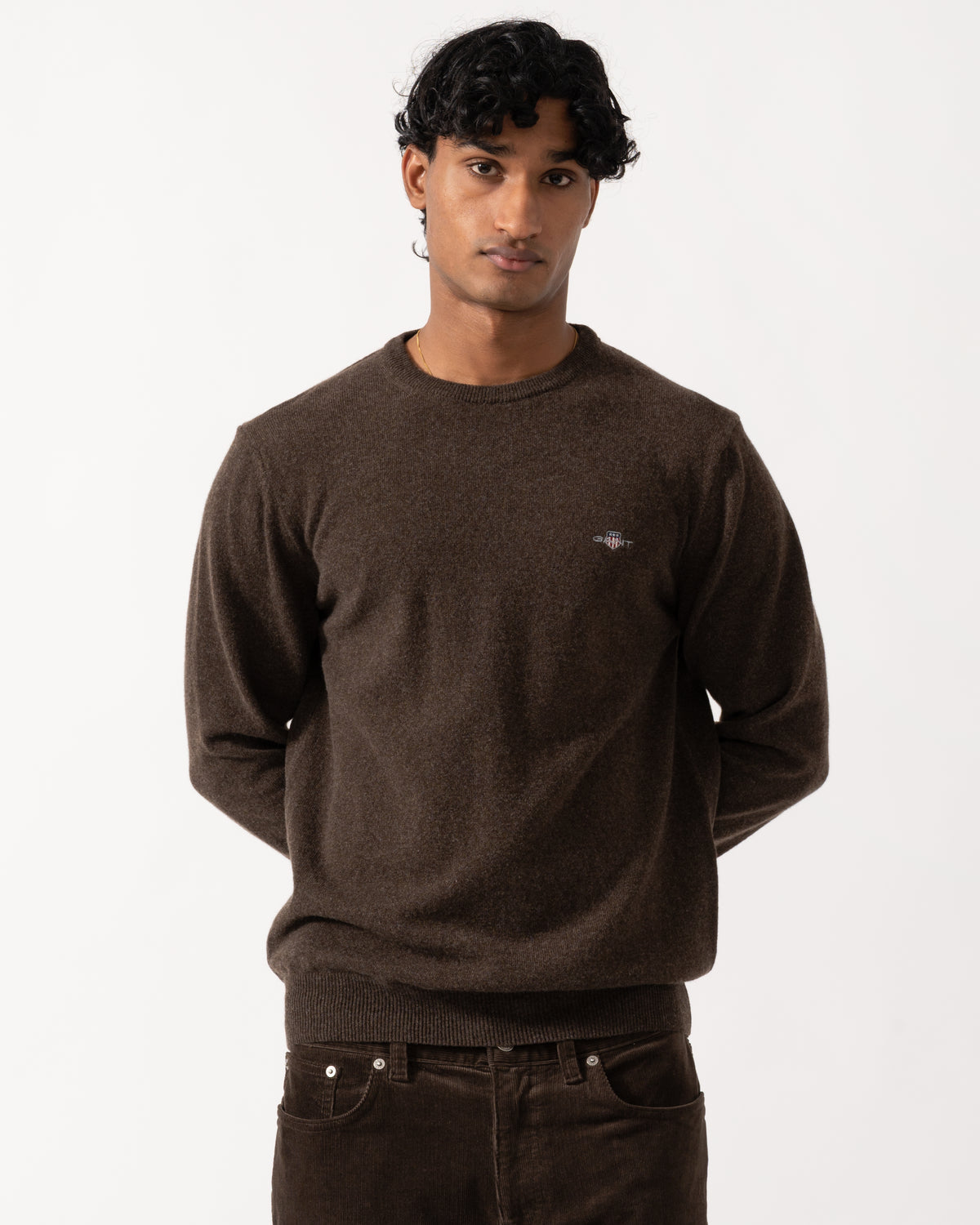 Studio photograph of a model wearing a GANT Mens Superfine Lambswool Crew Neck Sweater in 280 Dark Brown Melange