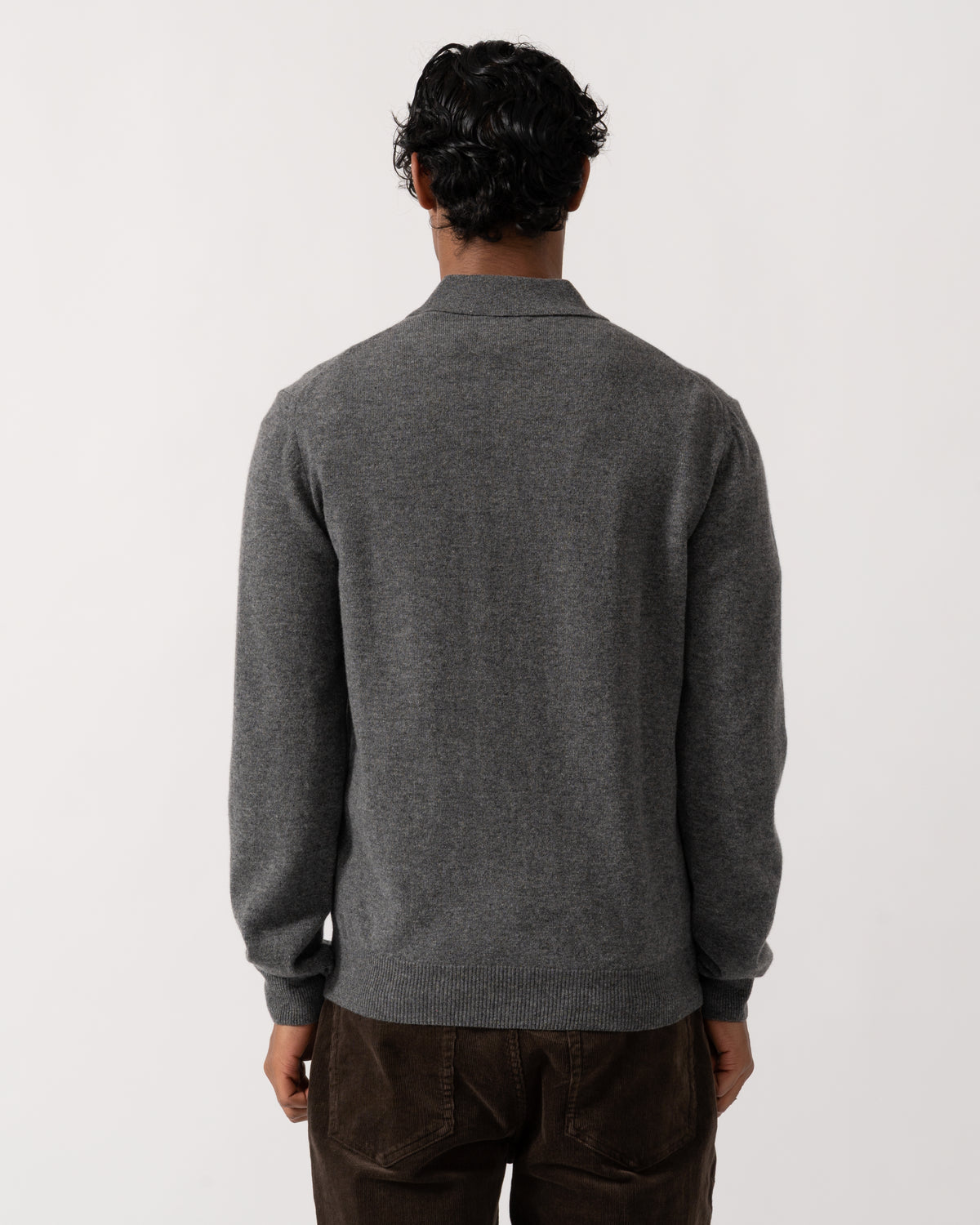 Studio photograph showing the back of a model wearing a GANT Mens Superfine Lambswool Long Sleeve Polo in 90 Charcoal Melange