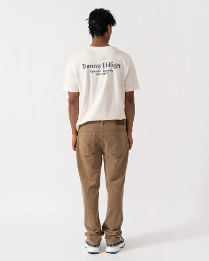 Model wearing the GANT Mens Regular Fit Cord Jeans - 264 Light Taupe and the  Tommy Hilfiger Mens Back Text Seasonal Graphic T-Shirt - Ivory Petal