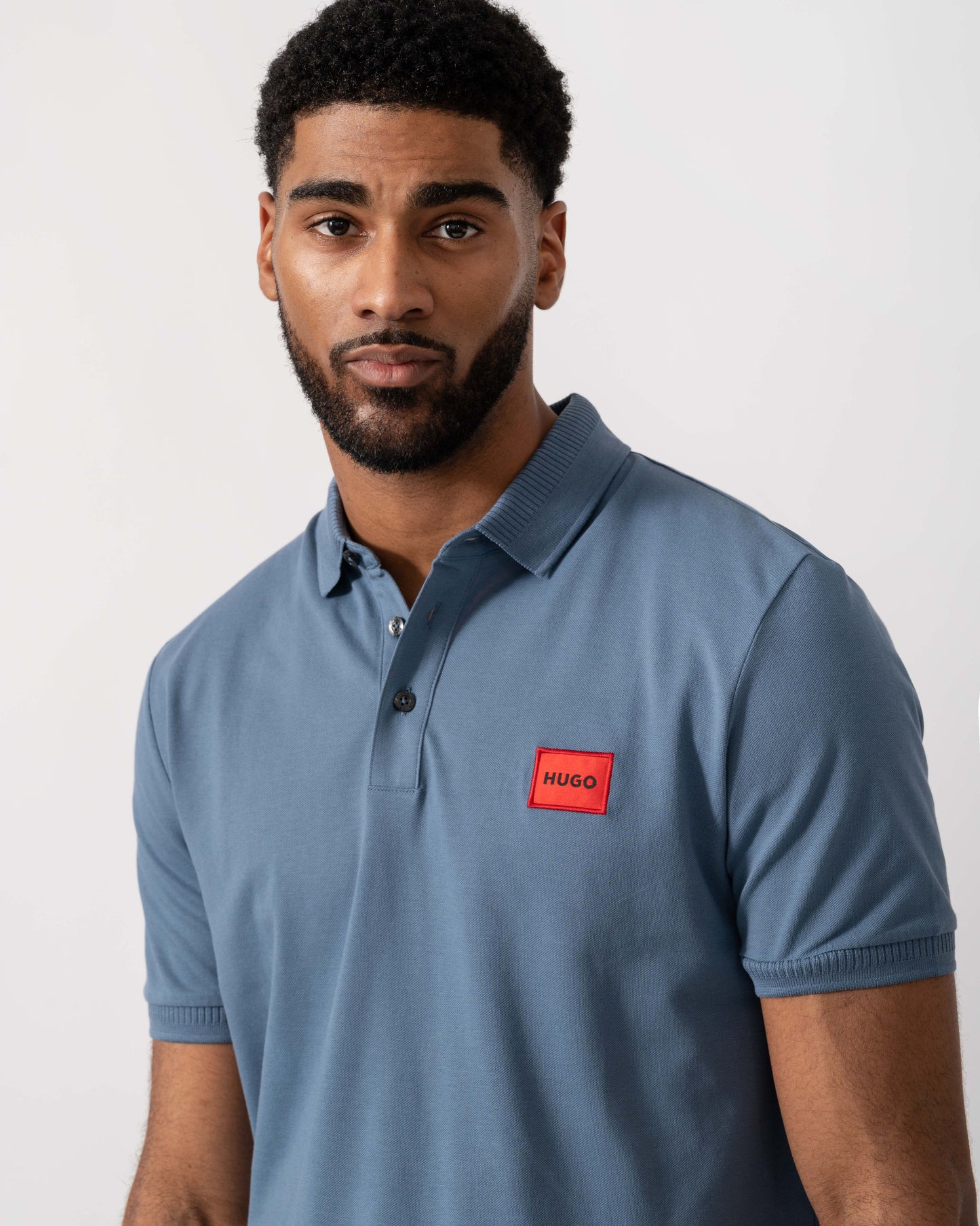 Model wearing HUGO Dereso222 Mens Cotton Piqué Slim-Fit Polo Shirt with Logo Label in Open Blue 496 - Detail