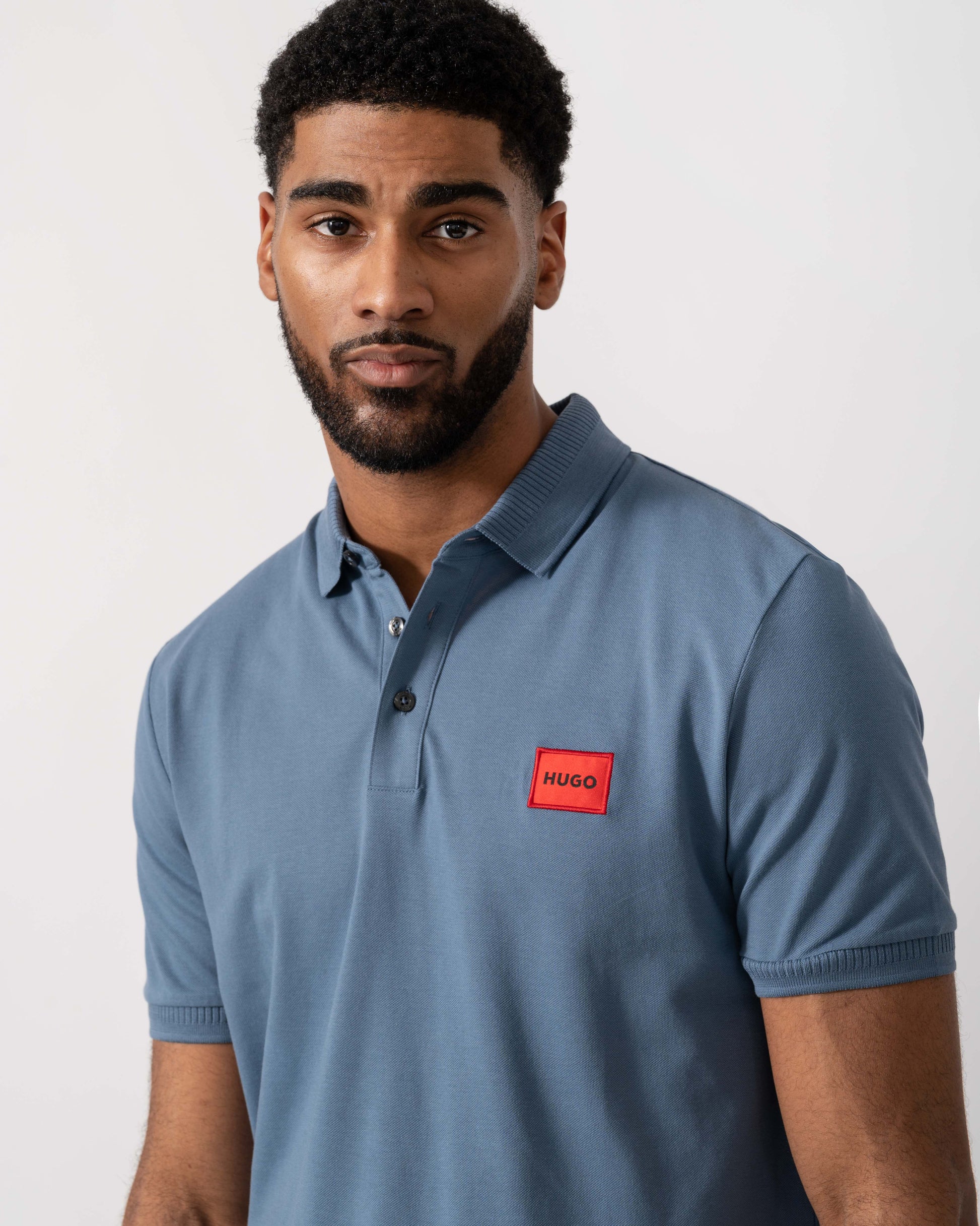 Model wearing HUGO Dereso222 Mens Cotton Piqué Slim-Fit Polo Shirt with Logo Label in Open Blue 496 - Detail