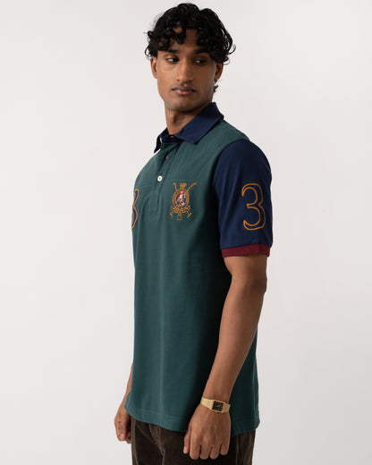 Studio photograph showing the side of a model wearing a Joules Woody Mens Embellished Polo Shirt in Green/Burgundy