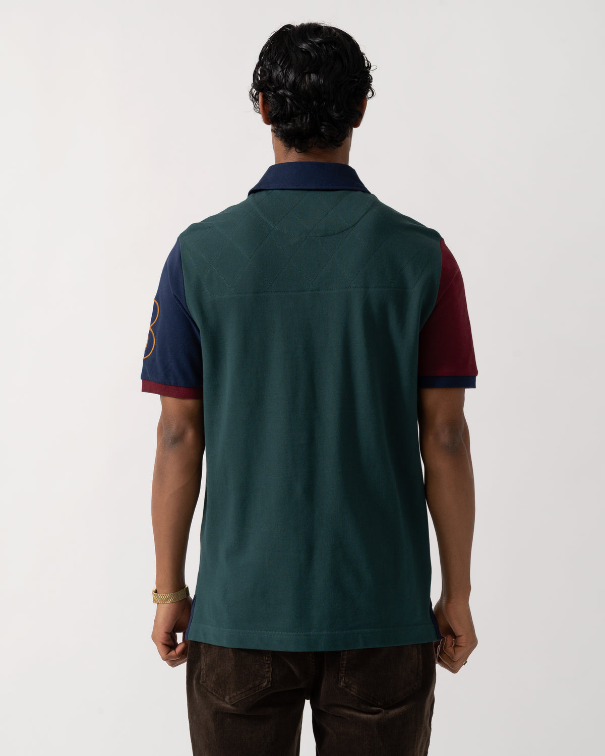 Studio photograph showing the side of a model wearing a Joules Woody Mens Embellished Polo Shirt in Green/Burgundy