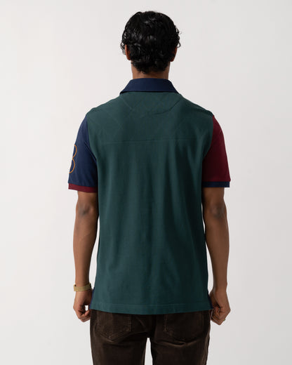 Studio photograph showing the side of a model wearing a Joules Woody Mens Embellished Polo Shirt in Green/Burgundy