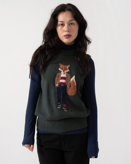A woman modeling a dark gray knit sweater vest with a detailed embroidered fox character on the front, layered over a navy blue long-sleeve shirt, against a plain light gray background.