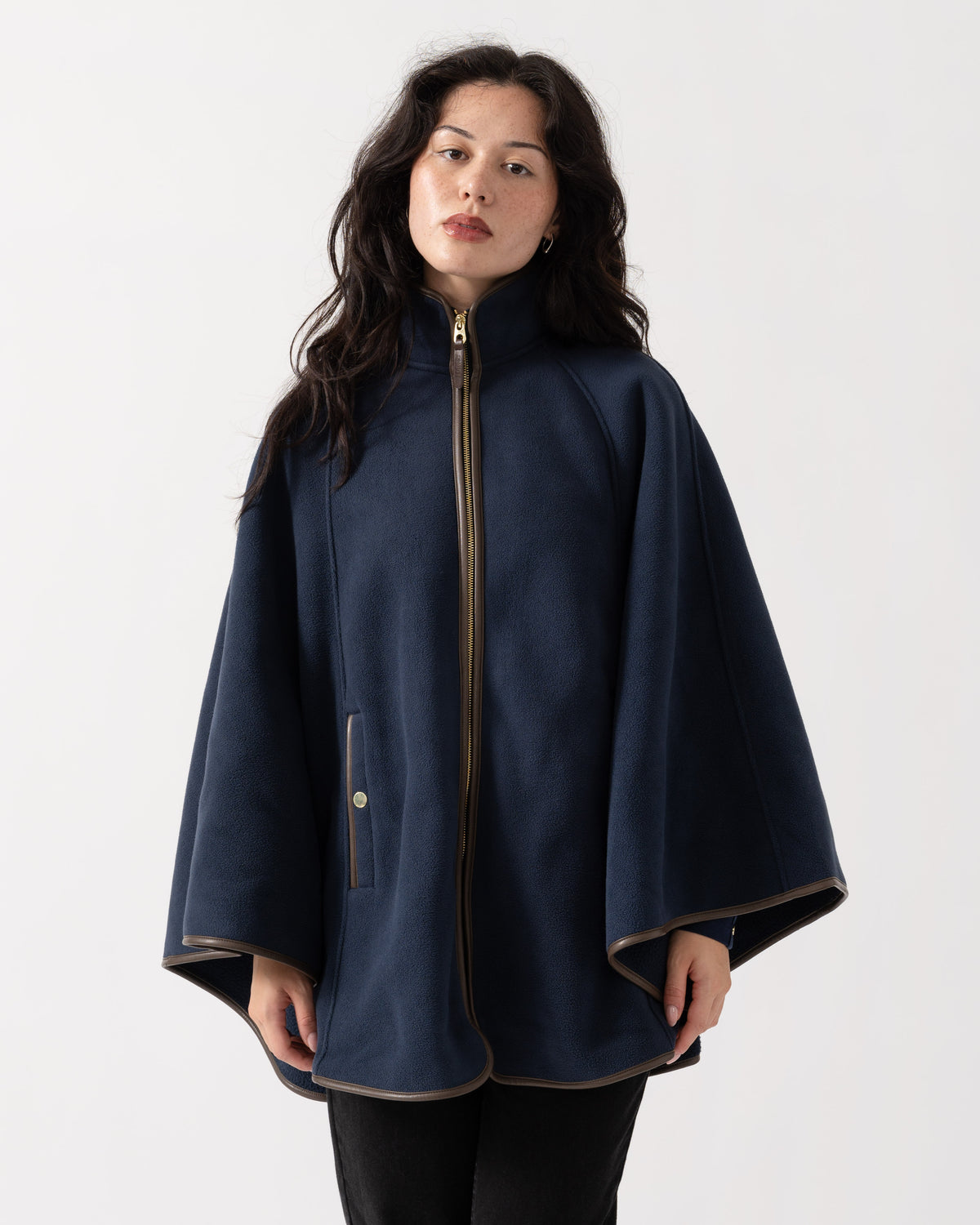 A woman wearing a navy blue cape-style coat with a high collar, front zipper, and wide draped sleeves, photographed against a plain light gray studio background.