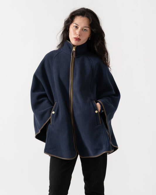A woman wearing a navy blue wool-blend coat with gold-toned trim and a front zipper, paired with black pants, photographed against a clean white studio background.