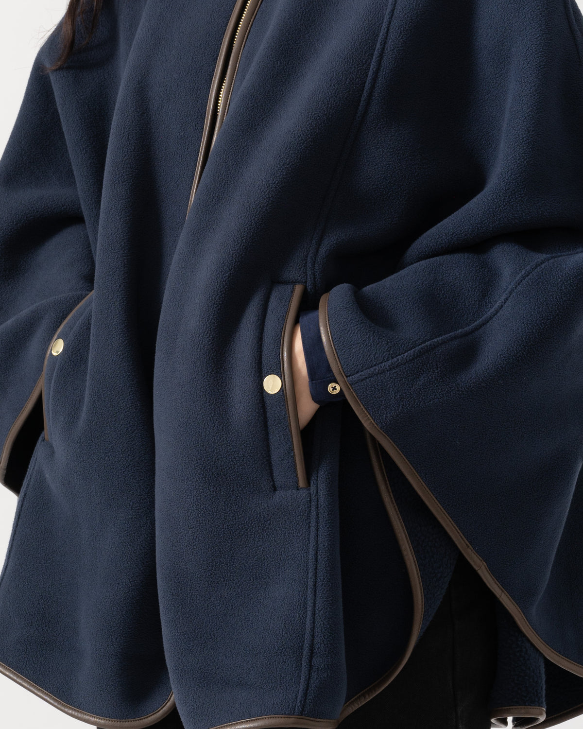 Close-up of a navy blue fleece jacket with brown contrast trim and gold-tone snap details, shown on a model.