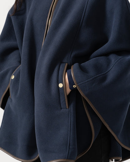 Close-up of a navy blue fleece jacket with brown contrast trim and gold-tone snap details, shown on a model.