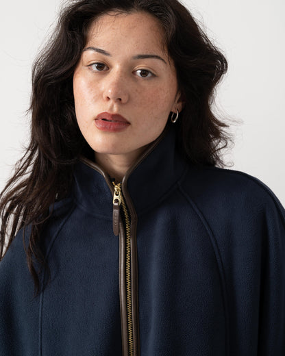 A close-up shot of a woman wearing a navy blue fleece jacket with a high collar and a gold-toned zipper. The background is a clean, neutral off-white studio setting.
