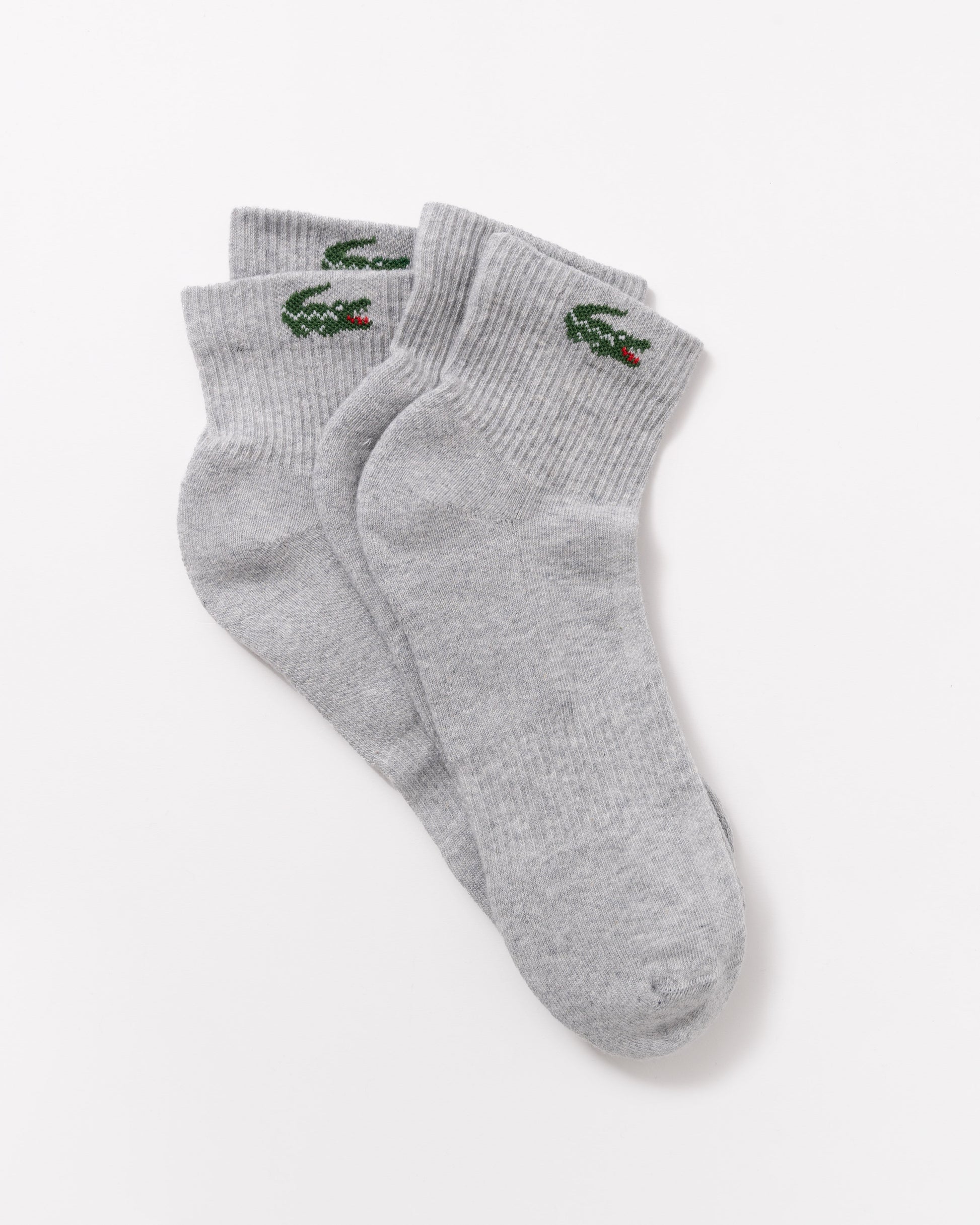 A pair of light gray heather crew socks with the green embroidered Lacoste crocodile logo on the cuff, displayed on a clean white background.