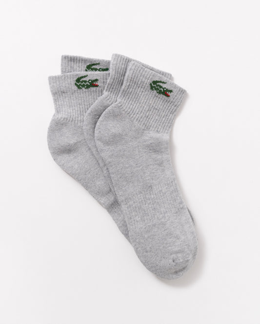 A pair of light gray heather crew socks with the green embroidered Lacoste crocodile logo on the cuff, displayed on a clean white background.