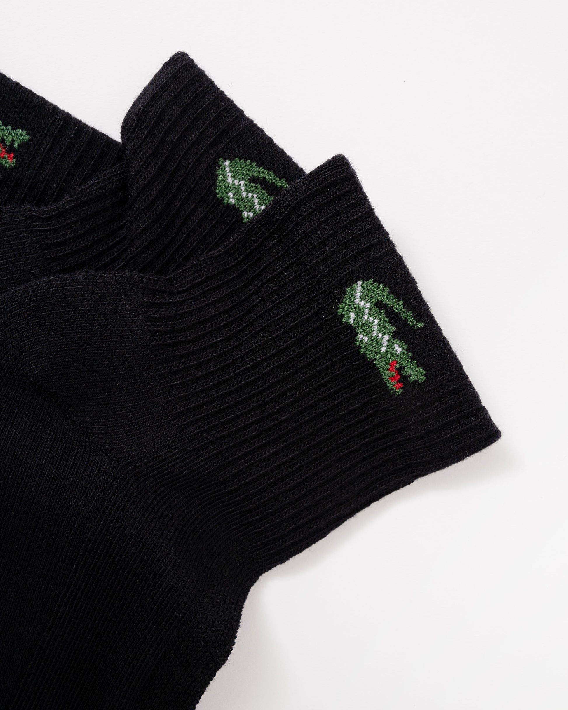 Black ribbed knit socks with green crocodile logos and small red accents on the cuffs, shown on a plain white background.