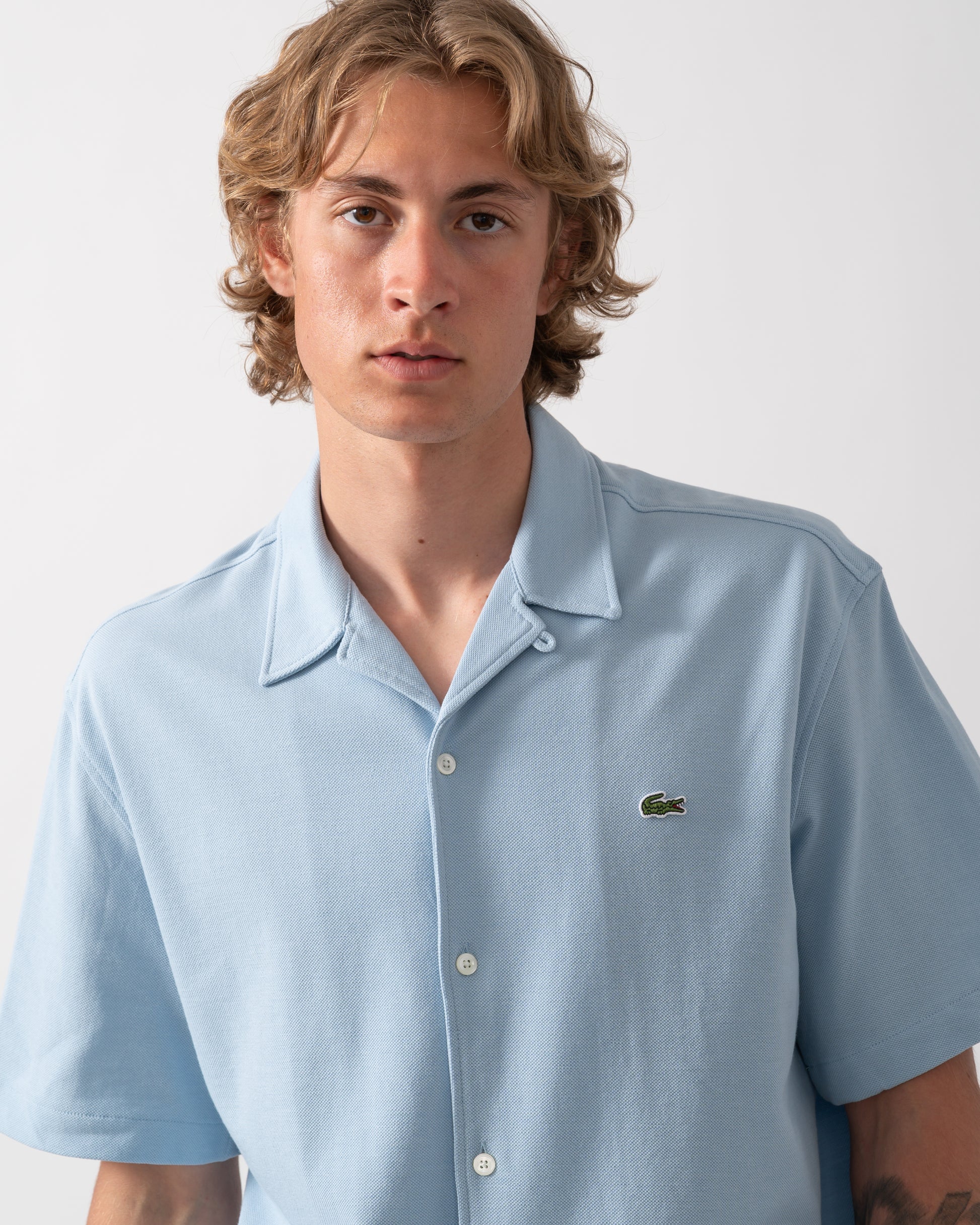 close up shot of a model wearing a Lacoste Relaxed Fit Short Sleeved Mens Piqué Shirt in Chambray HBA