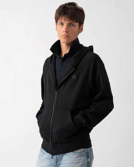 a model wearing a Moose Knuckles Mens Yul Zip Up Hoodie in Black 292