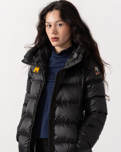 A woman wearing a black puffer jacket with a high collar over a navy blue top, photographed against a clean white studio background.