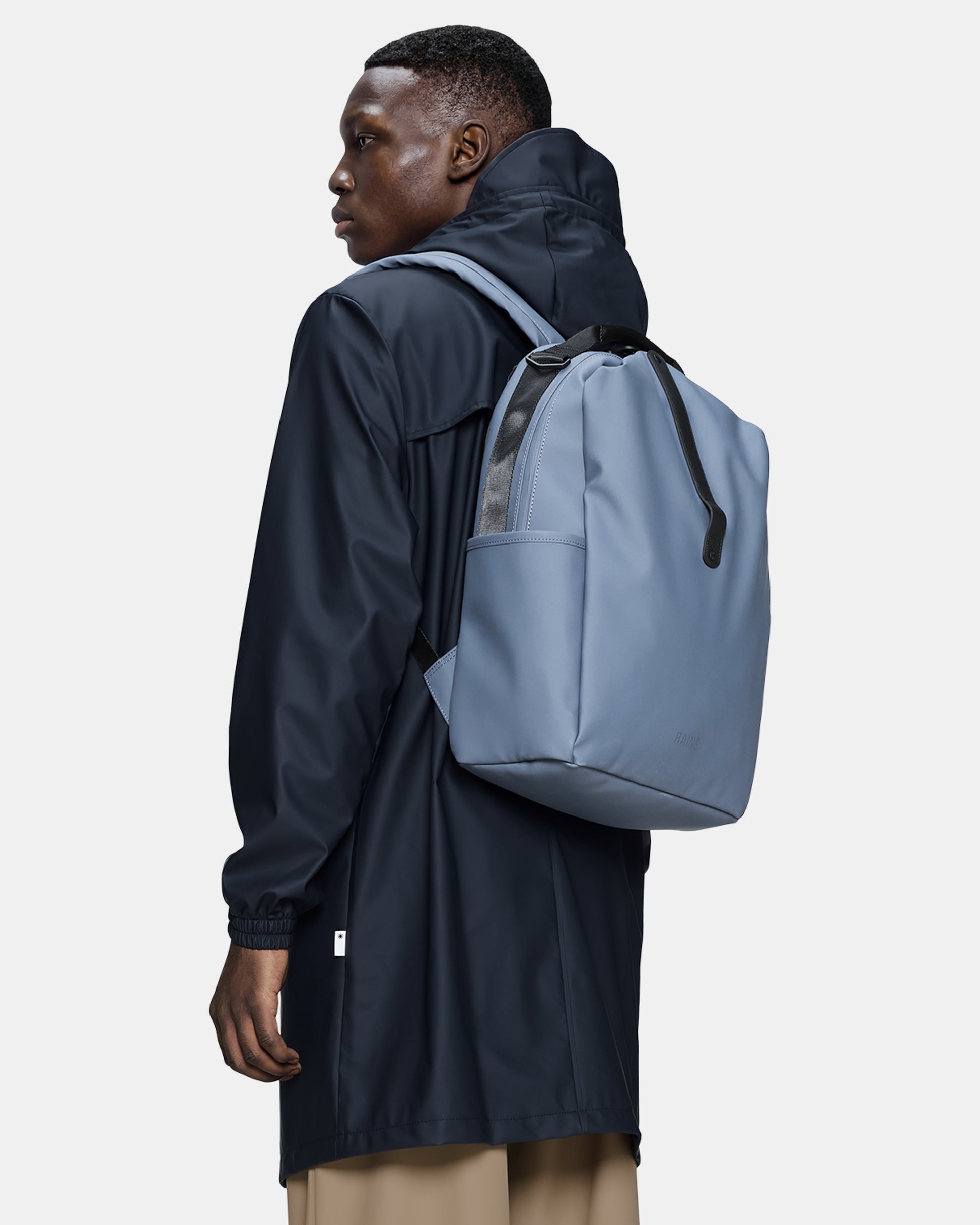 model carrying a Rains Clip Front Backpack in 172 Blue Dusk