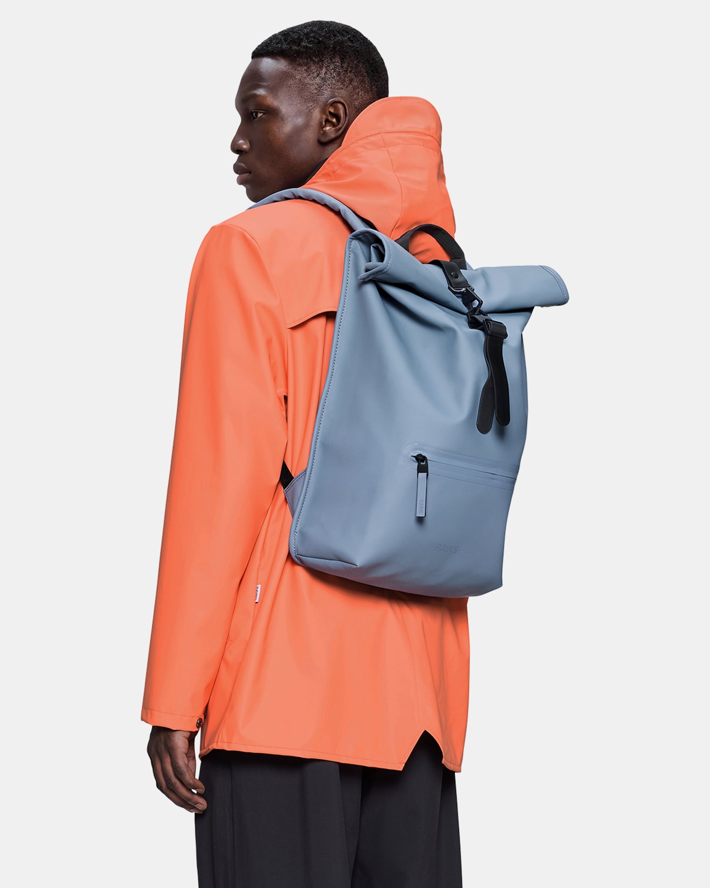 model carrying a Rains Unisex Rolltop Rucksack in 172 Blue Dusk