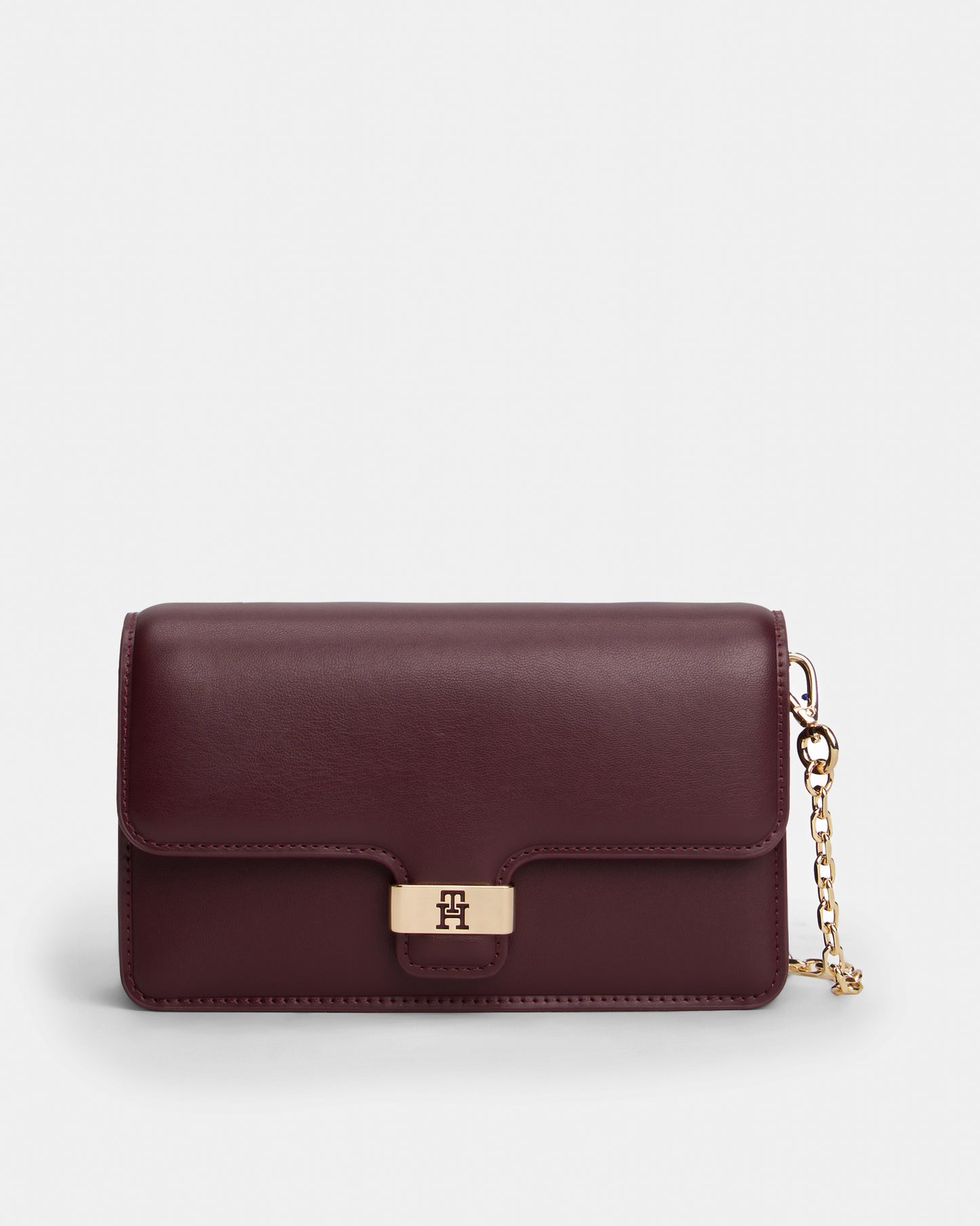 Burgundy Tommy Hilfiger handbag with a gold chain on a light grey background