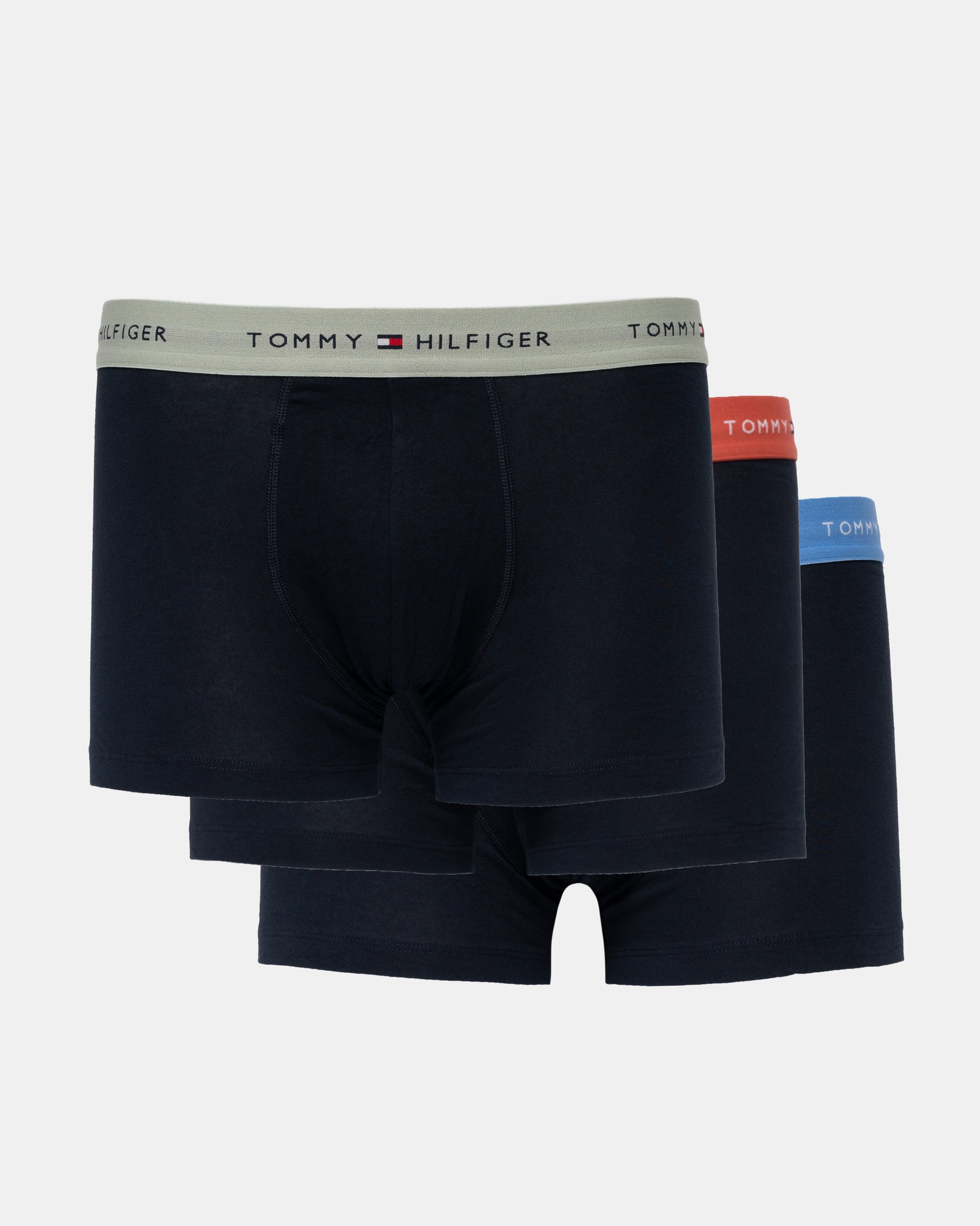 Three pairs of Tommy Hilfiger men's boxer briefs in dark navy blue, stacked together on a light gray background. The front pair has a light gray waistband with the Tommy Hilfiger logo, while the pairs behind it have red, orange, and blue waistbands.