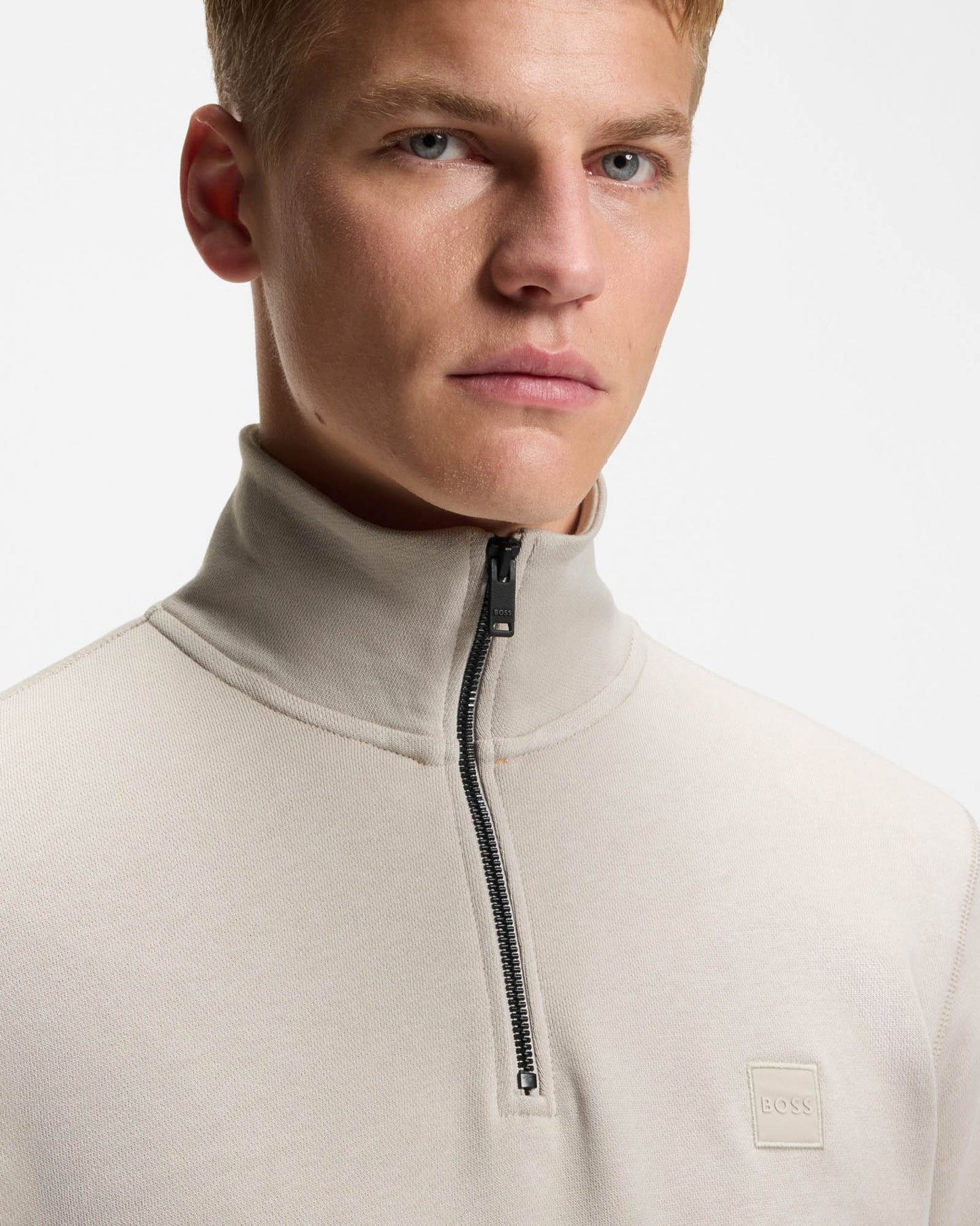 Man wearing a beige high-neck sweater with a zipper on a light gray background