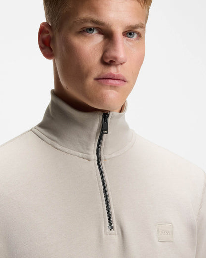 Man wearing a beige high-neck sweater with a zipper on a light gray background