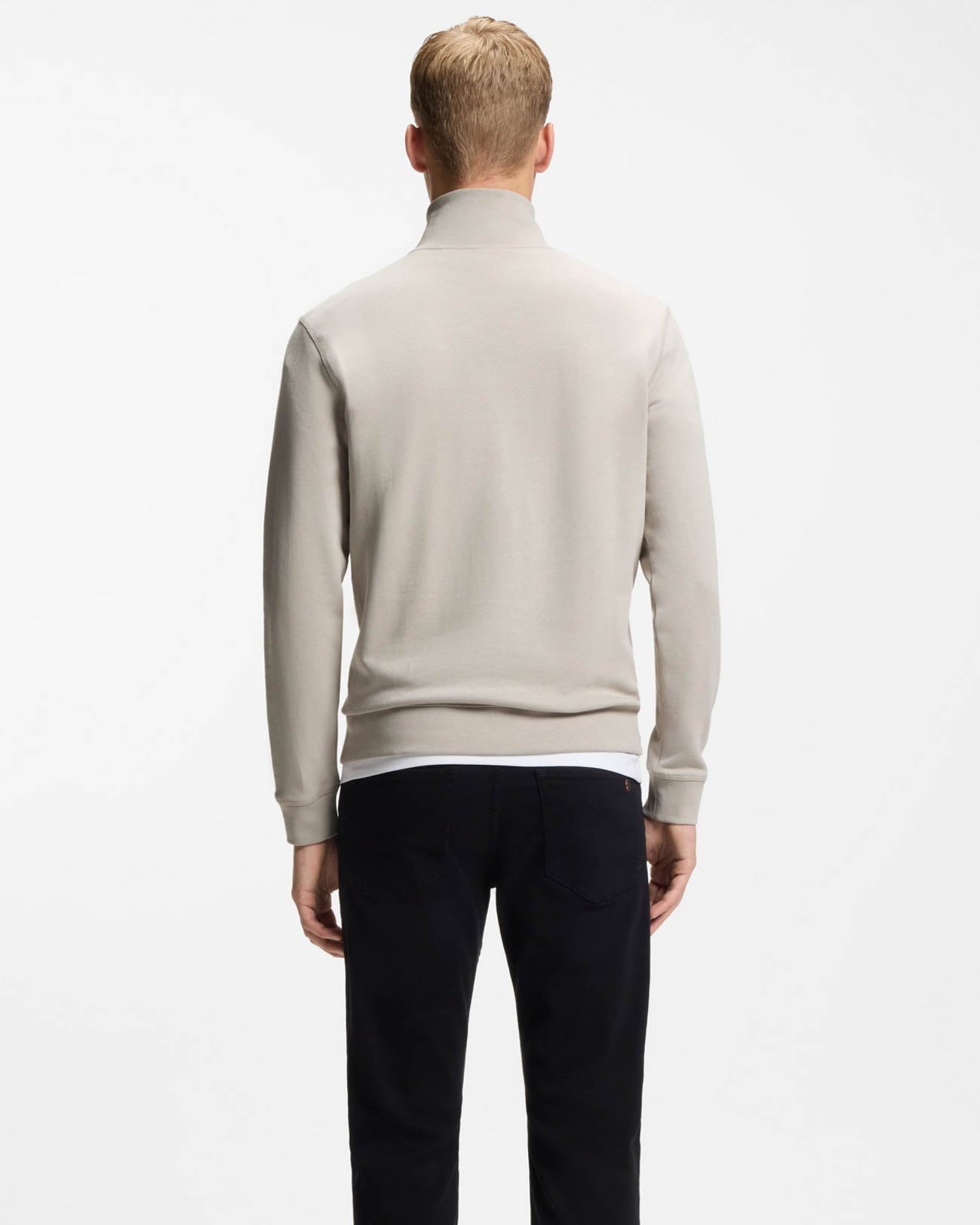 Man wearing a light gray sweater and dark pants on a white background