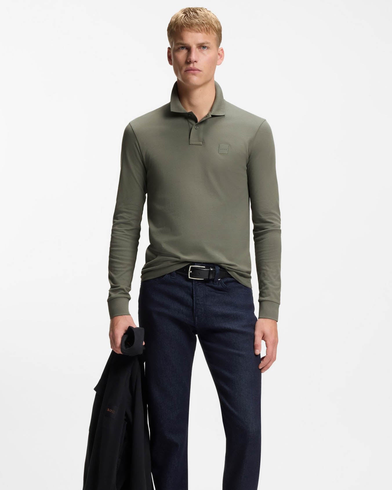 Man wearing a green long-sleeve BOSS polo shirt and dark pants on a white background